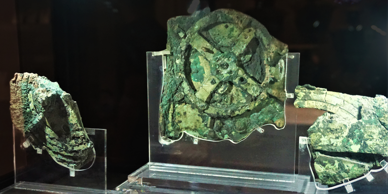 The three main surviving fragments of the Antikythera mechanism, corroded bronze mounted in display cases at the National Archaeological Museum, Athens