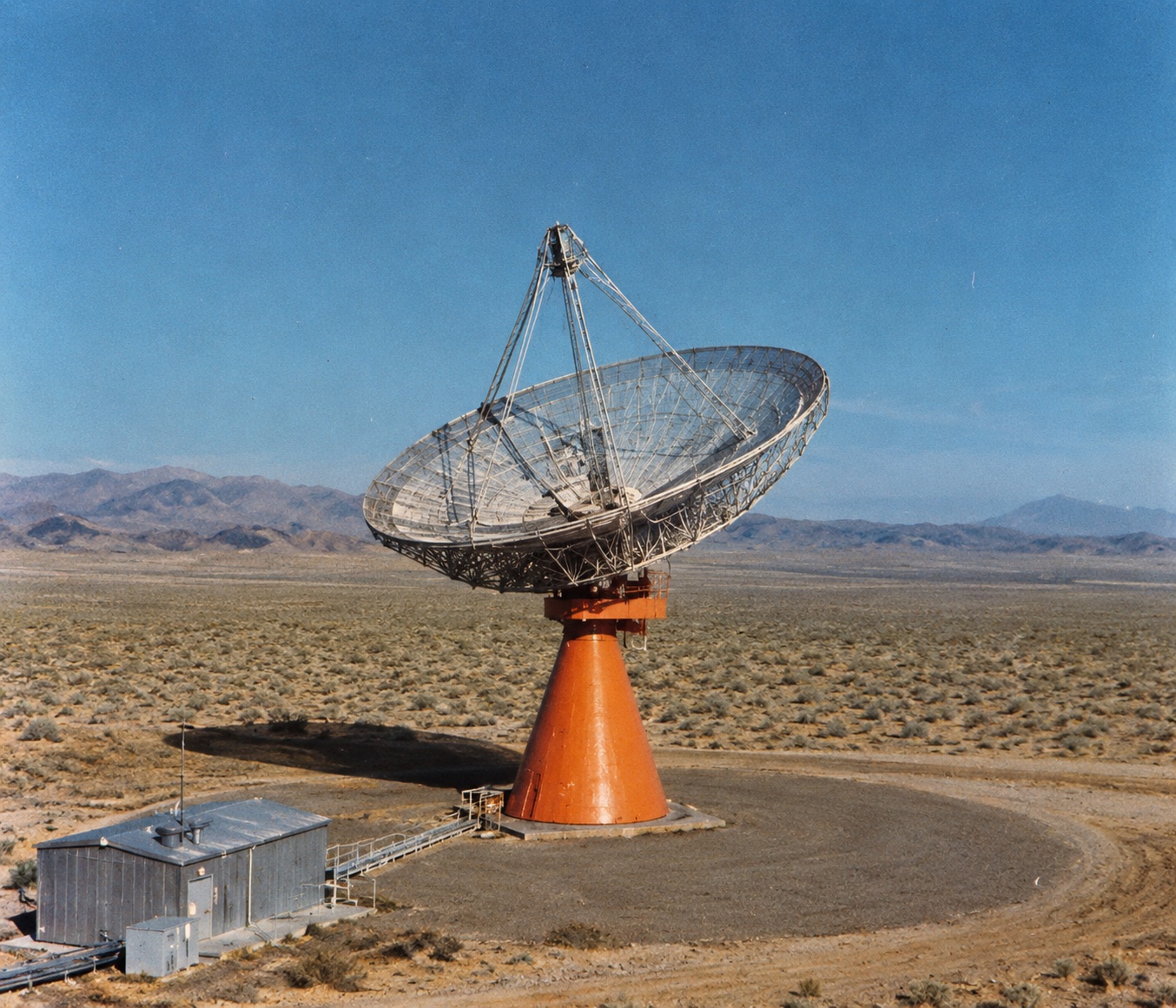 A large steerable radio dish on an orange pedestal mount in the Mojave desert, an early Goldstone tracking station antenna.